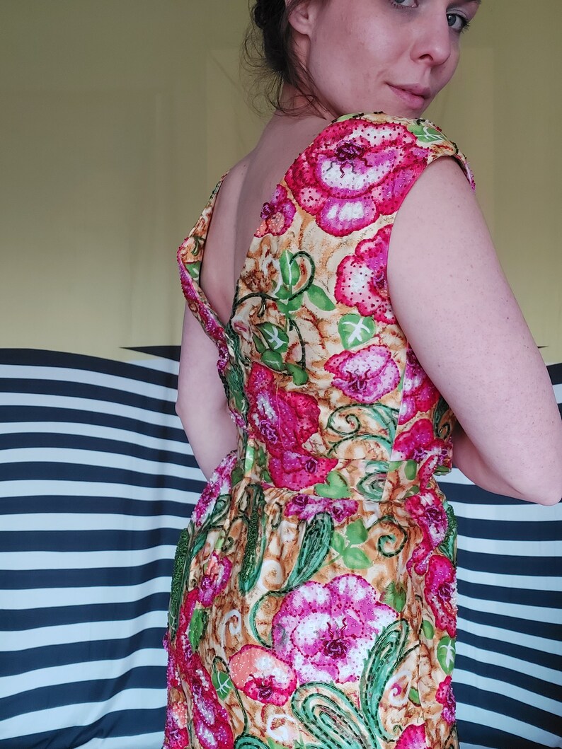 Op de afbeelding: Een mouwloze jurk met een bloemenpatroon in tinten roze, groen en geel. De jurk is gemaakt van een textuurrijke stof en heeft een diepe V-hals.