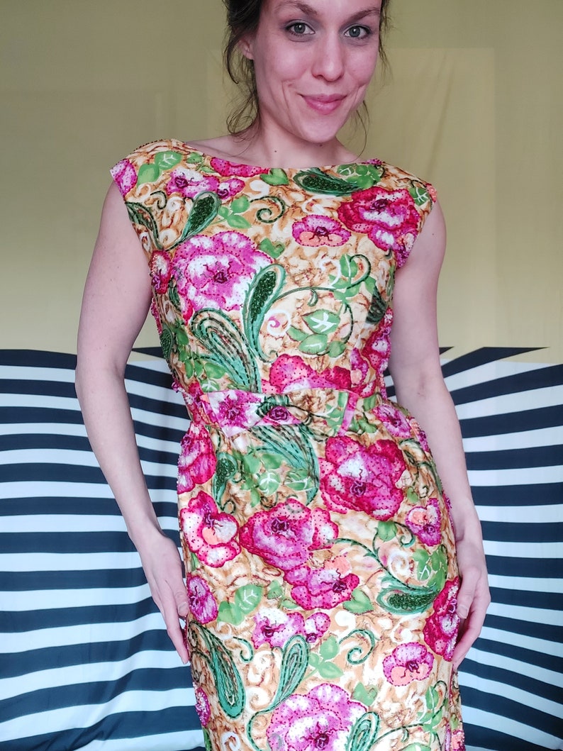 Op de afbeelding: Een mouwloze jurk met een bloemenprint in tinten roze, groen en goud. De jurk heeft een aansluitende pasvorm en een ronde hals.