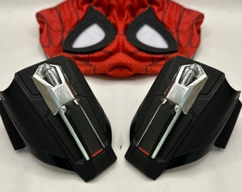 May include: A Spider-Man costume set featuring a red and black mask with white eye openings and two black wrist web shooters with silver accents and red details. The costume set is designed for cosplay or dress-up.