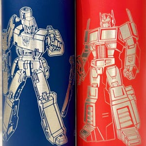 May include: Two insulated water bottles, one blue and one red, each featuring a silver-colored robot design. The blue bottle has a black lid, while the red bottle has a red lid. Both bottles are cylindrical and likely made of stainless steel.