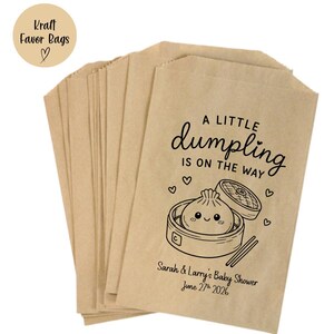 May include: Kraft favor bags with a cute dumpling illustration and the text "A Little Dumpling is on the Way." The bags are light brown and feature a baby shower announcement for Sarah & Larry's baby shower on June 27th, 2026.
