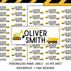 May include: A sheet of rectangular white adhesive labels featuring yellow construction vehicle graphics, the text THIS BELONGS TO, and the name OLIVER SMITH in bold black letters. The design includes a yellow excavator and a yellow dump truck.
