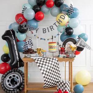 May include: A birthday party table setting with a checkered tablecloth, a black and white checkered gift box, a yellow balloon, and a cake decorated with a checkered pattern and the number "No. 1". The table is decorated with a checkered banner that says "Happy Birthday".