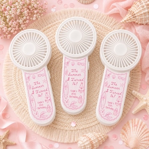 May include: Three white handheld portable fans featuring a pink printed design on the handle. The text reads The Summer I Turned 16! Sadie's 16th Birthday, accompanied by illustrations of a surfboard, bikini, beach bag, sunglasses, and waves.