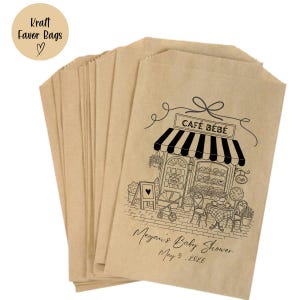 May include: Kraft favor bags in a stack, made of brown paper. Each bag features a black and white illustration of a cafe with the text "CAF&Eacute; B&Eacute;B&Eacute;". The bags are personalized with the text "Megan's Baby Shower May 9, 2026".
