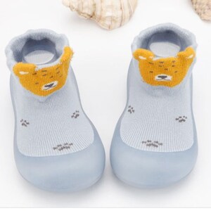 May include: A pair of light blue baby booties with a yellow bear face design on the front. The booties have a rubber sole and are made of soft, breathable fabric.