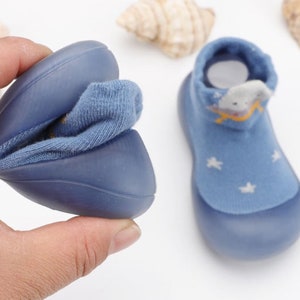 May include: A pair of blue baby shoes with a soft, stretchy fabric upper and a rubber sole. The shoes feature a star pattern and a cartoon cloud design.