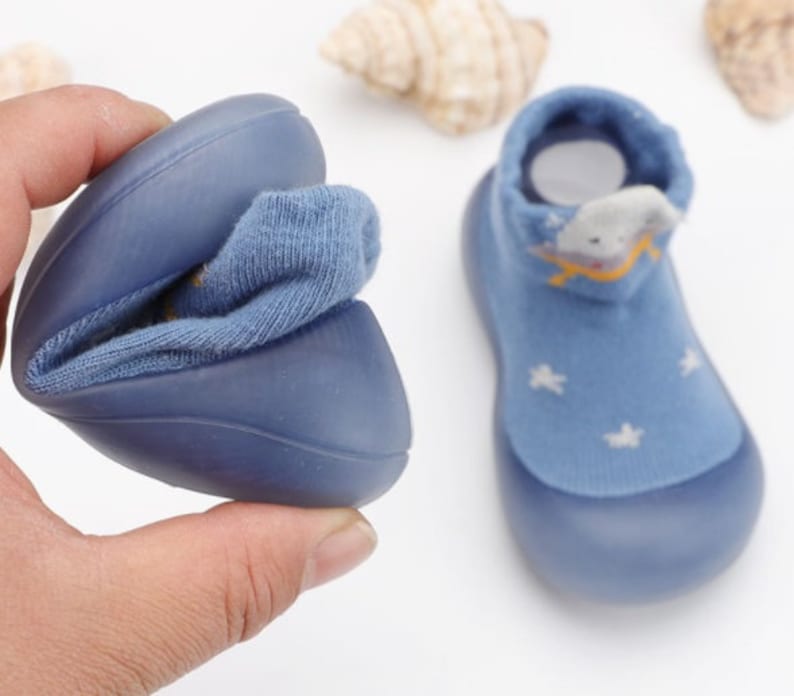 May include: A pair of blue baby shoes with a soft, stretchy fabric upper and a rubber sole. The shoes feature a star pattern and a cartoon cloud design.