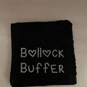 May include: A black towel, folded and featuring the text "B❤️ll❤️ck Buffer" in silver glitter. The towel is made of a soft, absorbent material.
