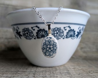 Może przedstawiać: Srebrny łańcuszek z białym porcelanowym wisiorkiem z niebieskim wzorem kwiatowym. Wisiorek ma kształt łzy i zwisa z srebrnego łańcuszka.