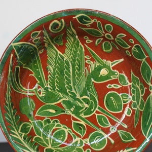 May include: A set of terracotta bowls with green and yellow painted designs. The bowls feature a stylized bird with outstretched wings and floral motifs.