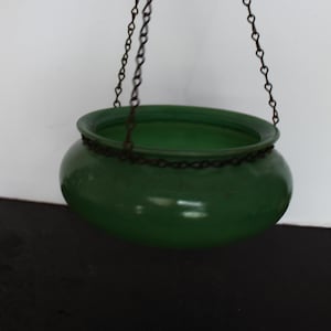 May include: A green hanging planter with a rounded shape, suspended by a dark metal chain. The planter has a glossy finish and a wide opening. The chain is attached to the rim of the planter.