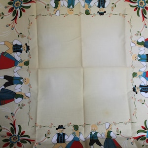 May include: A white tablecloth with a blue border and a colorful folk art design. The design features a repeating pattern of flowers, leaves, and people in traditional clothing dancing around the border.