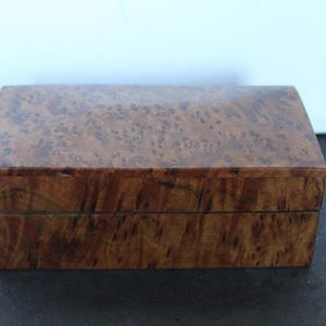 May include: A rectangular wooden box with a hinged lid. The box is made of a dark brown wood with a burl pattern on the top and sides. The box is sitting on a dark surface.