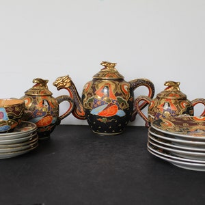 May include: A black and gold Japanese tea set with intricate floral and geometric designs. The set includes a teapot, creamer, sugar bowl, and two teacups and saucers.
