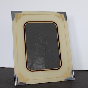 May include: A rectangular photo frame with a cream-colored border and a dark gray interior. The frame has a thin, dark red border around the inner rectangle and silver metal corner accents. Vertical gold lines decorate the cream border.
