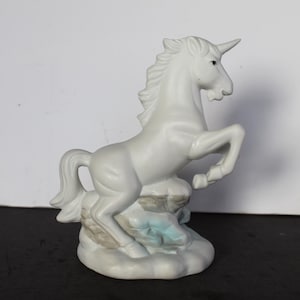 May include: A white ceramic unicorn figurine rearing up on a cloud-like base. The unicorn has a long horn, flowing mane, and is posed as if it is about to leap. The base has light blue and gray accents.