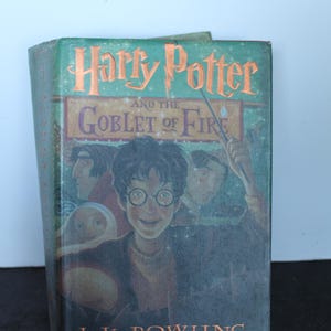 May include: A hardcover book titled "Harry Potter and the Goblet of Fire" by J. K. Rowling. The cover features a green background with orange lettering and illustrations of characters from the story. The book is slightly worn.
