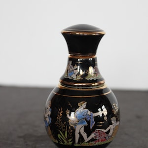May include: A black ceramic vase with a gold rim and lid. The vase features a classical Greek design with figures in blue, red, and gold. The vase is a decorative item.