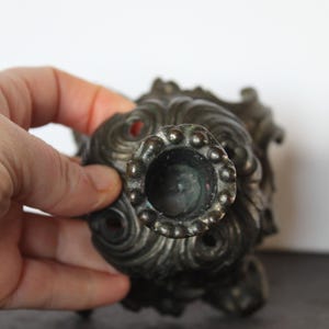 May include: Ornate, antique bronze candlestick holder with a detailed, swirling design. The candle holder has a circular opening and a decorative, textured surface. The overall design is reminiscent of a vintage, classical style.
