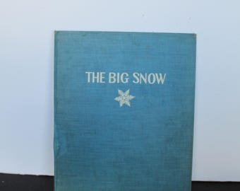 Può includere: Un libro con copertina rigida blu intitolato THE BIG SNOW con un grafico a fiocco di neve bianco centrato sotto il testo. La copertina presenta una finitura ruvida simile al tessuto e il titolo è stampato in un carattere bianco semplice.