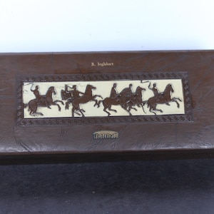 May include: A rectangular brown box with a textured surface featuring a central cream-colored panel with a dark brown relief of figures riding horses. The text R. Inglehart is printed above the panel, and the word Thermold is printed below it.