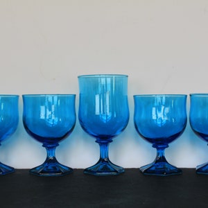 May include: Set of six blue glass goblets with a square base. The goblets are all the same size and shape, and they have a clear, smooth surface.