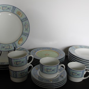 May include: A set of blue and white ceramic dinnerware with a sea life design. The set includes a large dinner plate, a smaller salad plate, a soup bowl, and a teacup and saucer. The plates and bowls feature a blue and white border with a pattern of fish, seashells, and starfish. The teacup and saucer have a similar design, but the teacup has a handle.