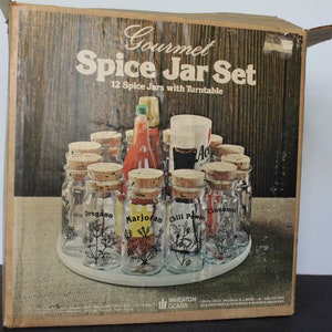 May include: A Gourmet Spice Jar Set with 12 spice jars and a turntable. The jars are clear glass with cork stoppers and labels for oregano, marjoram, chili powder, and cinnamon. The set is in a cardboard box with a wood-grain design.