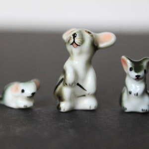 May include: Three small ceramic figurines of mice. The mice are white with black and green accents. One mouse is standing on its hind legs with its front paws raised. Another mouse is sitting on its hind legs with its front paws resting on its belly. The third mouse is sitting on its hind legs with its front paws raised.