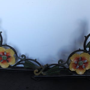 May include: A decorative, cast iron shelf bracket with a floral design. The bracket is painted black with yellow, red, and green accents on the flowers and leaves. The bracket is approximately 12 inches wide.