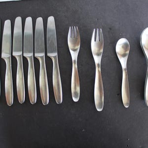 May include: A set of silver cutlery, including knives, forks, and spoons. The cutlery is arranged in a row on a dark surface.