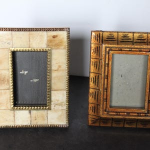 May include: Two decorative picture frames. One frame has a cream-colored, mosaic-like border with a gold inner frame and a dark gray interior. The other frame is gold with a geometric pattern and a light gray interior.