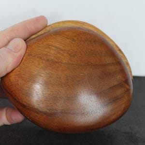 May include: A smooth, rounded wooden bowl with a polished finish, showcasing a rich, warm brown grain pattern. The object has a curved, organic shape with a deep, concave center and a glossy, reflective surface that highlights the natural wood texture.