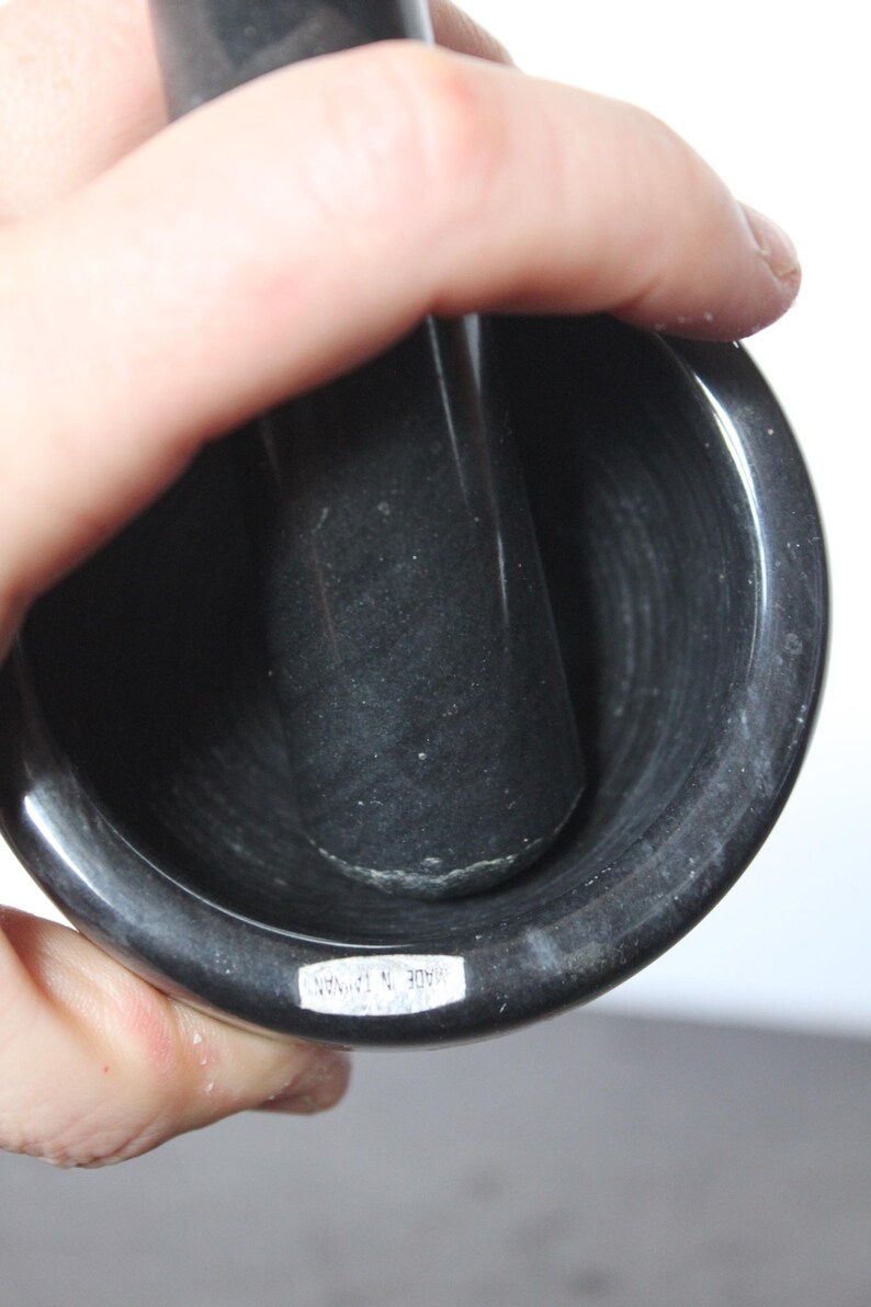 May include: A black mortar and pestle set. The mortar is a deep bowl shape, and the pestle is a cylindrical shape. The set is made of a dark, possibly stone material. The text "MADE IN TAIWAN" is visible on the mortar.