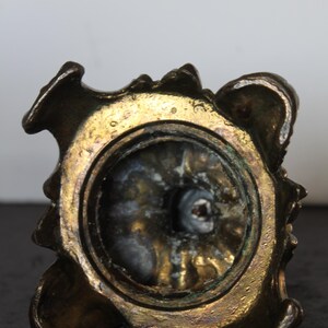 May include: Close-up of a bronze-colored, ornate object with a circular opening. The object has a textured, aged appearance with gold and dark brown tones. The design features a decorative, possibly floral, pattern around the rim.