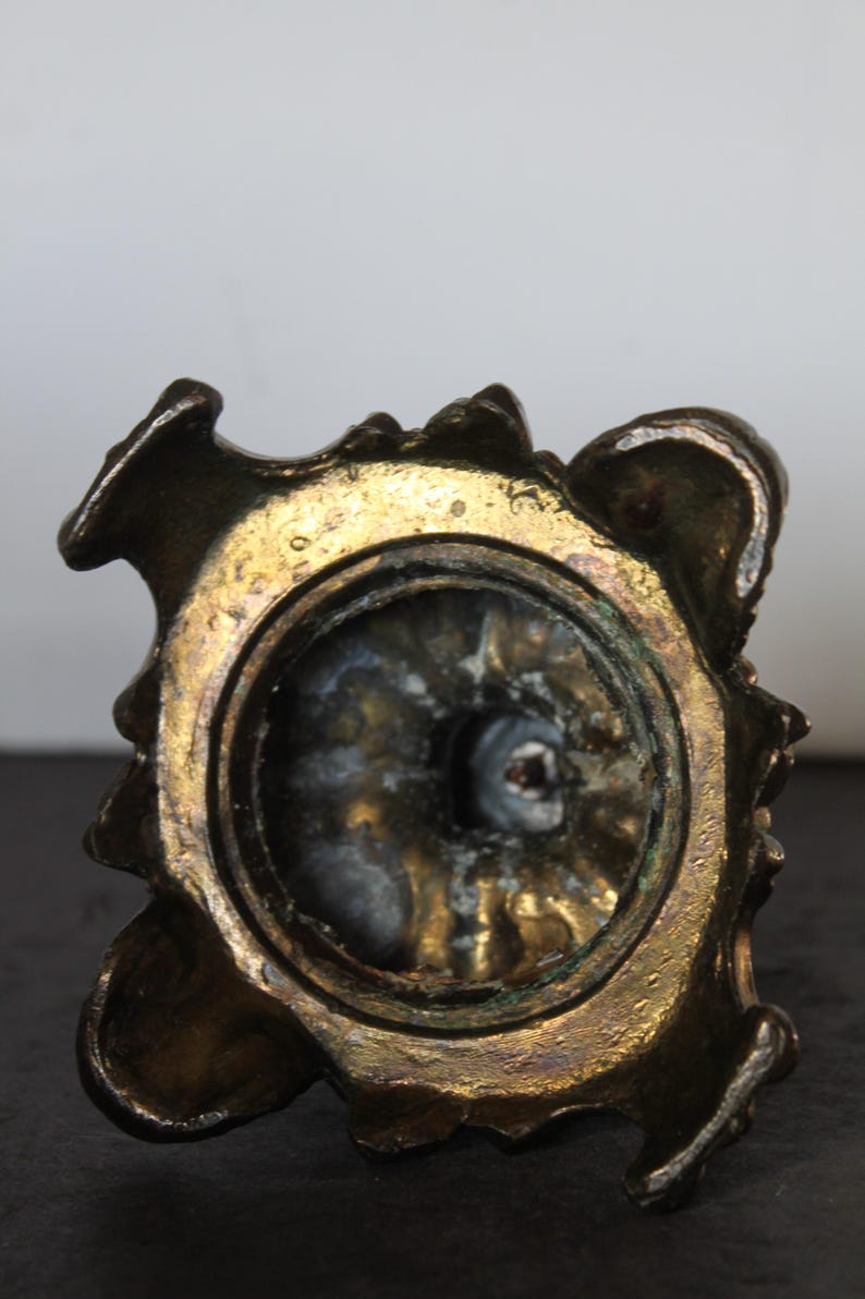 May include: Close-up of a bronze-colored, ornate object with a circular opening. The object has a textured, aged appearance with gold and dark brown tones. The design features a decorative, possibly floral, pattern around the rim.