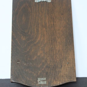 May include: A dark brown wooden plaque with a scalloped edge and a metal hook on the back. The plaque has two small nails on the bottom edge.