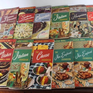 May include: A collection of vintage cookbooks with colorful covers featuring various cuisines, including German and Viennese, Southern and Southwestern, Chocolate, Italian, Hungarian, Scandinavian, Quick Dishes, Italian, Cheese, New England, and French.