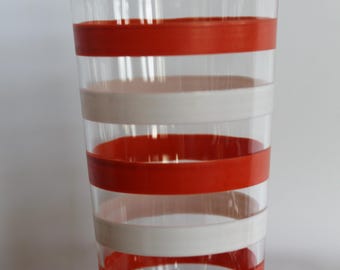 May include: Clear glass tumbler with horizontal red and white stripes. The glass is cylindrical and appears to be part of a set. The stripes are evenly spaced, creating a retro design. The glass is empty.