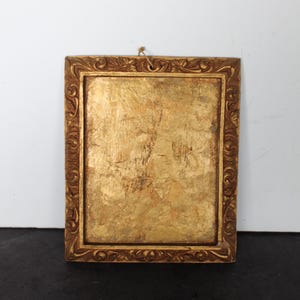 May include: A rectangular wall frame featuring a heavily textured, metallic gold finish. The border displays an intricate, carved scrollwork pattern. The central panel is flat and finished in a distressed, mottled gold leaf effect with a small hanging loop.