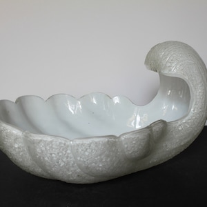 May include: A white glass bowl shaped like a seashell with a textured surface.