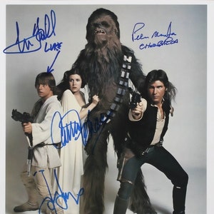 May include: A signed photograph of the cast of Star Wars: A New Hope. The actors are Harrison Ford, Carrie Fisher, Mark Hamill, and Peter Mayhew. The signatures are in blue ink.