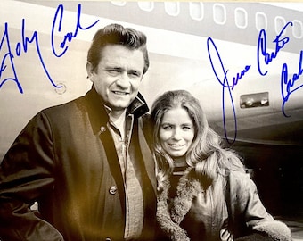May include: Black and white photo of Johnny Cash and June Carter Cash, both smiling, with their autographs in blue ink.