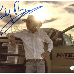 May include: An autographed photograph featuring a man in a cowboy hat and sunglasses, leaning against a truck. He wears a white button-down shirt and jeans. The truck has the text "M-TEX CO." on the side. The signature is in blue ink.