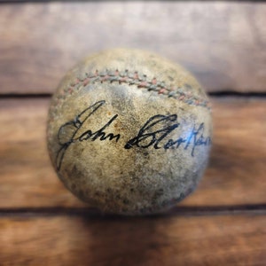 May include: A worn, white baseball with red stitching and the signature "John  Brant" in black ink.