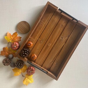 May include: A wooden tray with black metal handles. The tray is filled with fall decor, including small pumpkins, pinecones, and fall leaves.
