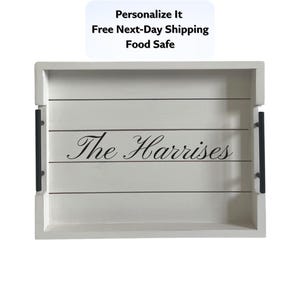 May include: A white wooden serving tray with black handles and the name "The Harrises" in elegant script. The tray has a rectangular shape with horizontal wooden slats. The text "Personalize It" is at the top.
