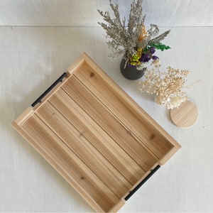 May include: A rectangular wooden tray with black metal handles. The tray has a light wood finish and is made of natural wood.