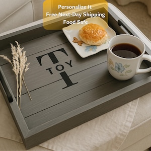 May include: A gray wooden serving tray with black handles and the word "TOY" in black letters. The tray holds a mug of coffee, a small plate with a pastry, and decorative wheat stalks. The tray is food safe.